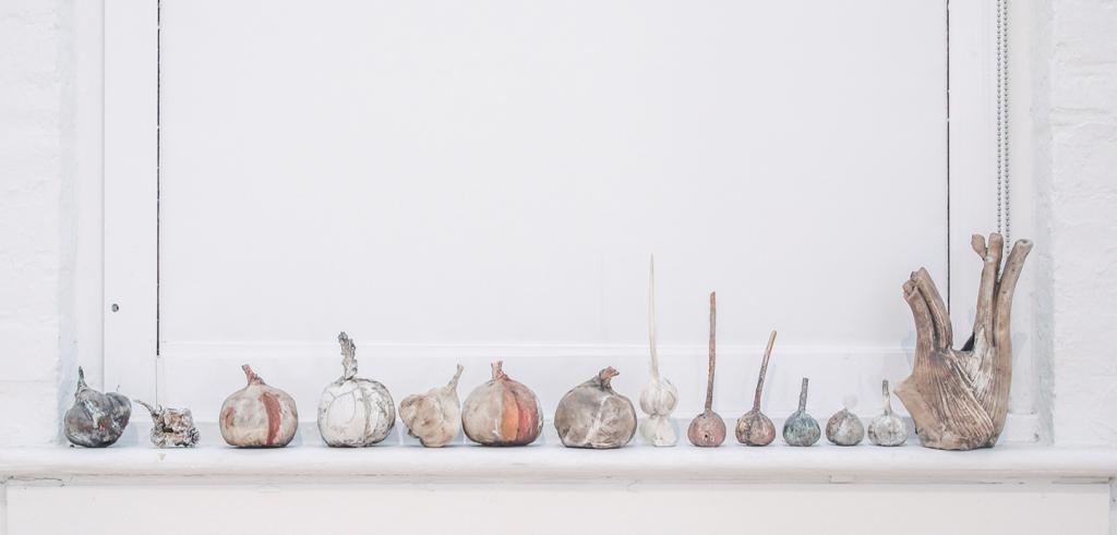 14 varying sculptures of turnips in white, orange and grey colors in a row on a white window sill 