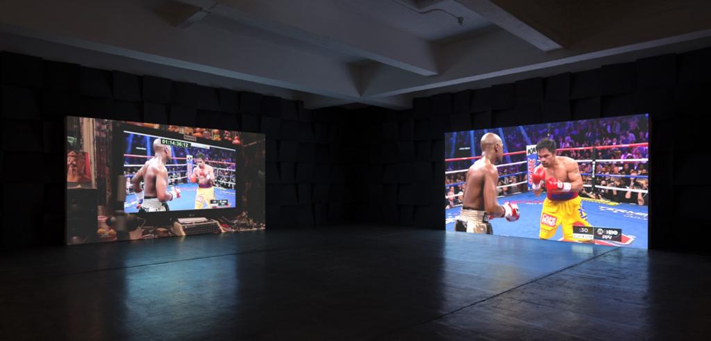 A dark room with two large screens with different projections of a boxing match on them. 