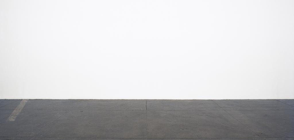 Blank white wall with a dark gray cement floor with a faded yellow line to the left.