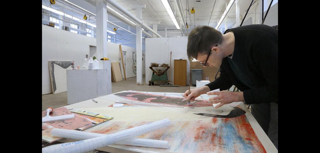 Man coloring on a piece of paper in the middle of a large workspace.