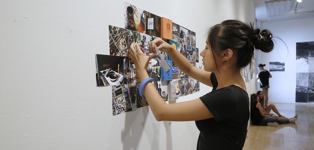 A student pins rectangular photographs to a white wall in a gallery