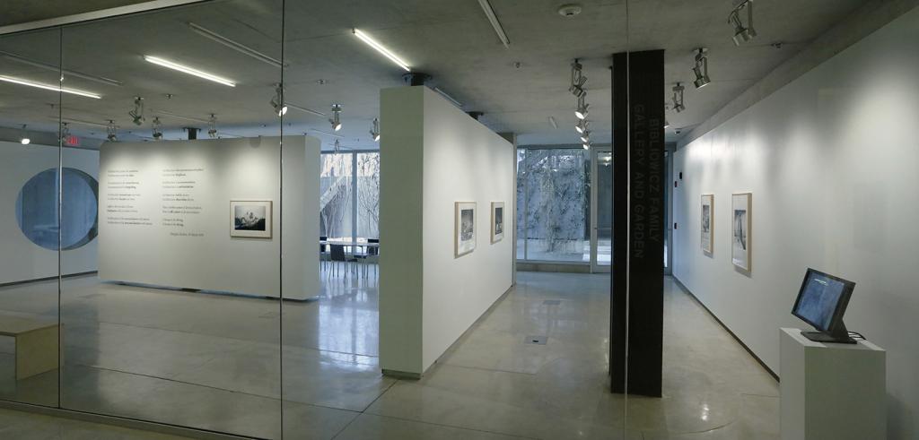 Galss and white gallery walls with framed images and text and a computer monitor on a pedestal.