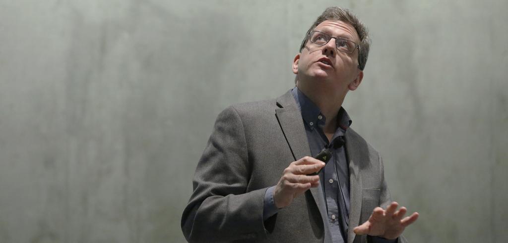 Man with glasses in front of concrete wall looking up.