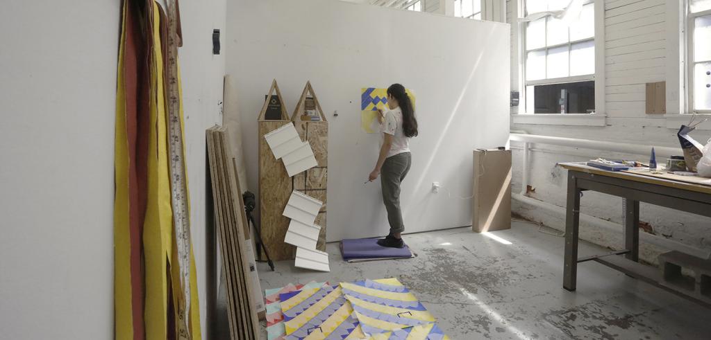 Woman with long dark hair working on a yellow and purple drawing in her studio.