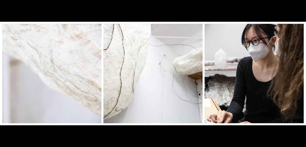 Two masked people examining cream colored abstract artwork. 