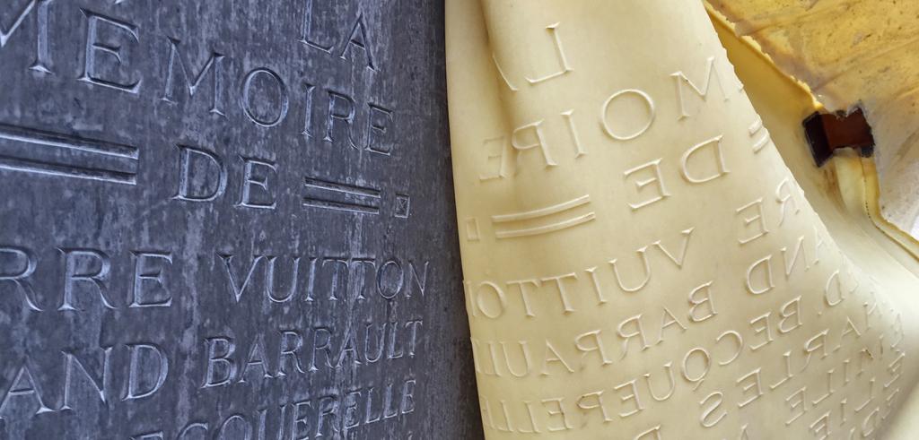 A flexible cast being peeled back from a bronze plaque memorial carved with latin text.