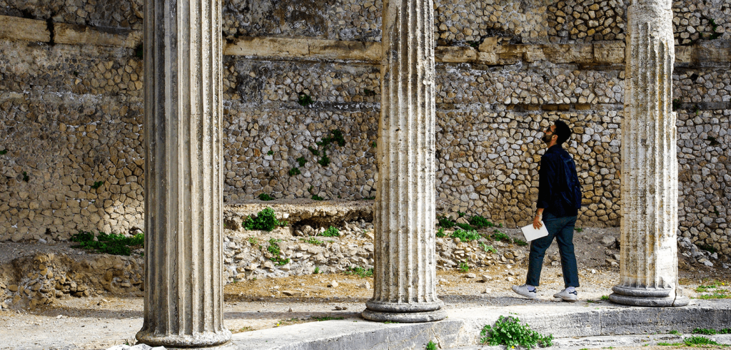 A person standing with a piece of paper in their hand peering up at a large pillared structure.