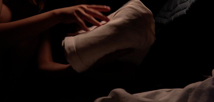 Two hands about to set down a folded white blanket on top of another white blanket against a dark background.