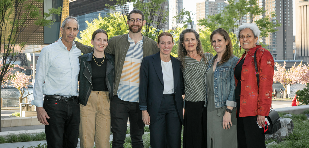 seven people standing next to each other with large buildings behind them