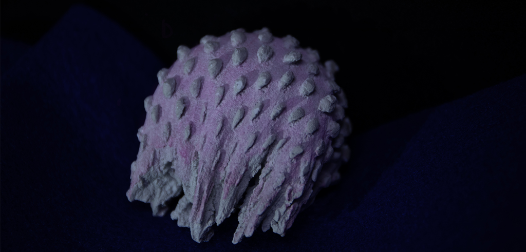 Photo of a purple cement sculpture with scale-like texture on a black background. 