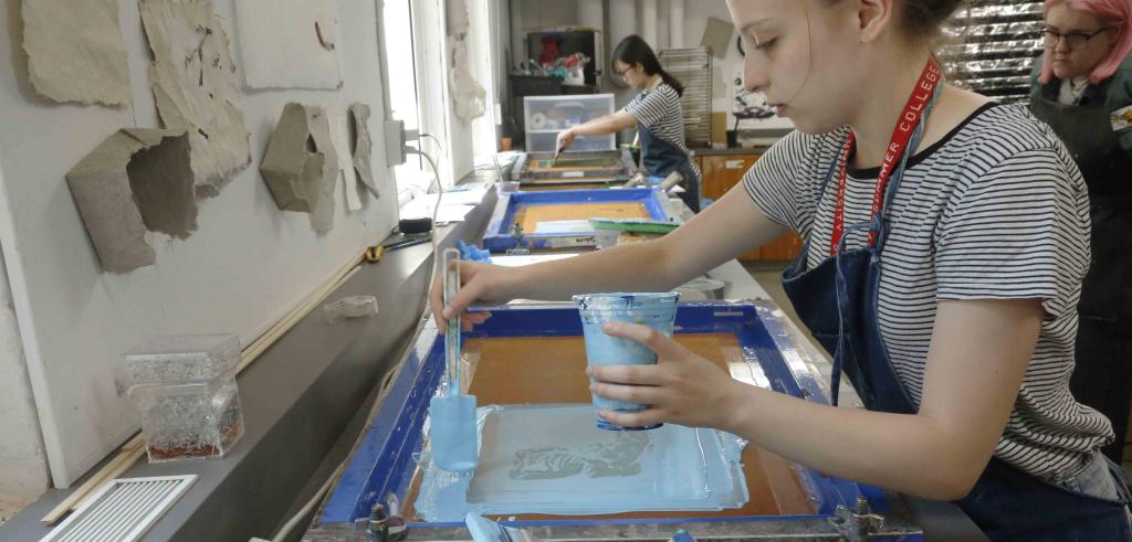 Two students in striped shirts with blue aprons working on screen printing.