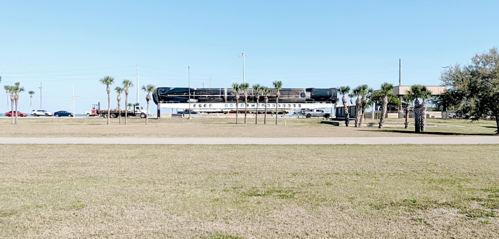 A rocket on a platform next to trees and grass and a sidewalk.