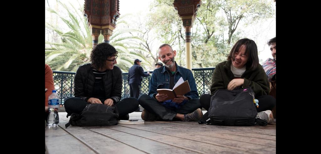 Three people sitting on the ground examining a book while others look on in the background.