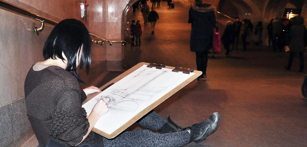 student sitting on the floor and sketching in train station