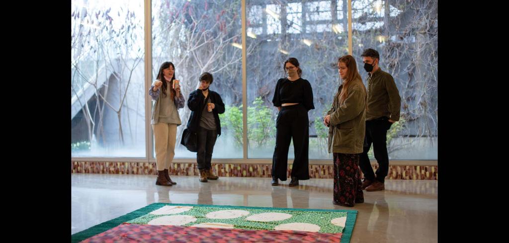 Five people gathered around a tapestry on the ground.