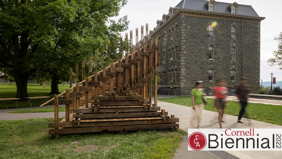 People walking on a sidewalk next to a wooden structure with a building in the background.