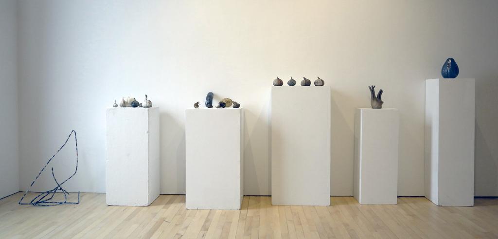 Clay and metal casts of various root vegetables on white pedestals.