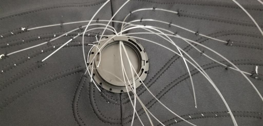A close up image of a grey plastic connector embedded in dark grey fabric, with clear wires extending outside the image border.