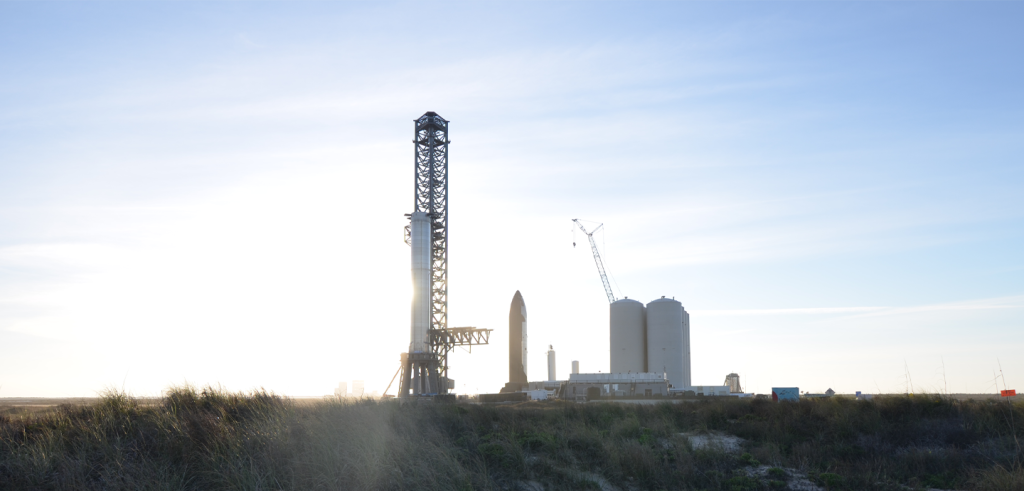 A large rocket next to a launch tower with crane in the distance.