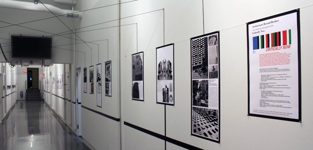 exhibition shot of black and white and colored posters on a wall with black tape above and below