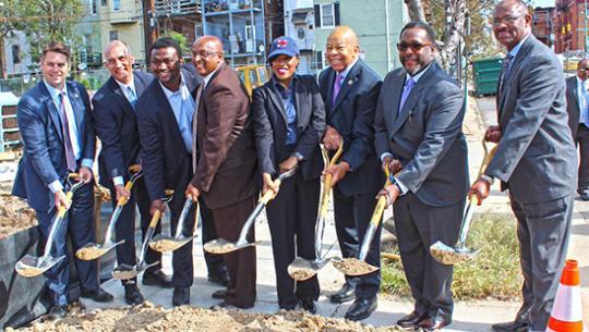 men and one woman in suits breaking ground on a site by ceremoniously shoveling dirt