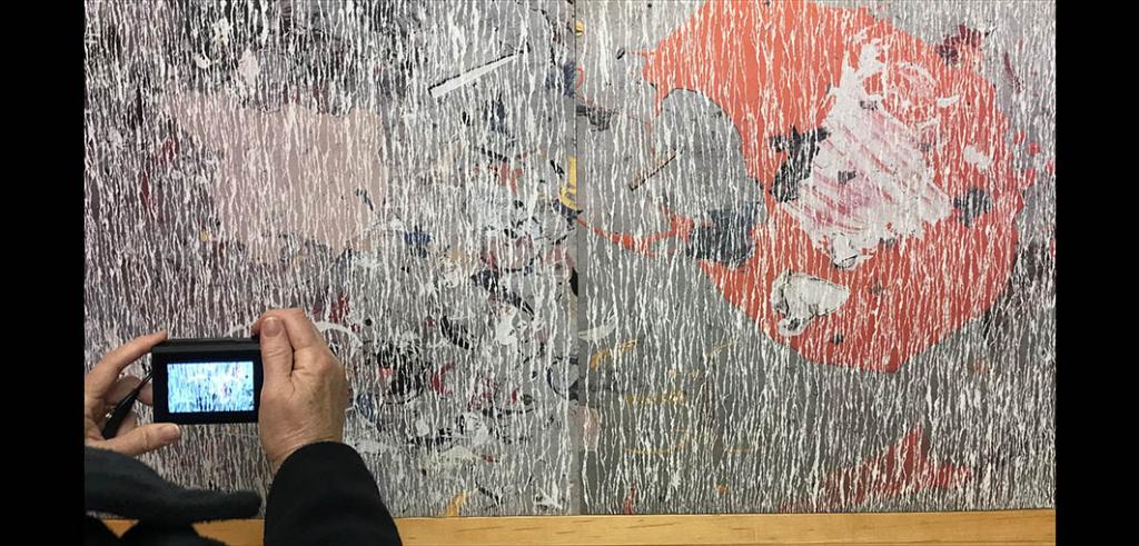 Someone's hands using a digital camera to photograph an abstract painting.