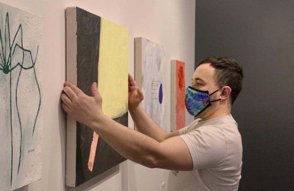 Person hanging a painting on a gallery wall.