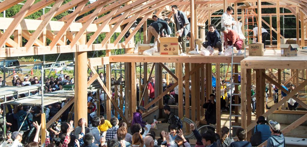 A group of individuals situated in a wood framed structure, consisting of a lower level filled with people, and loft area where fewer stand above. 