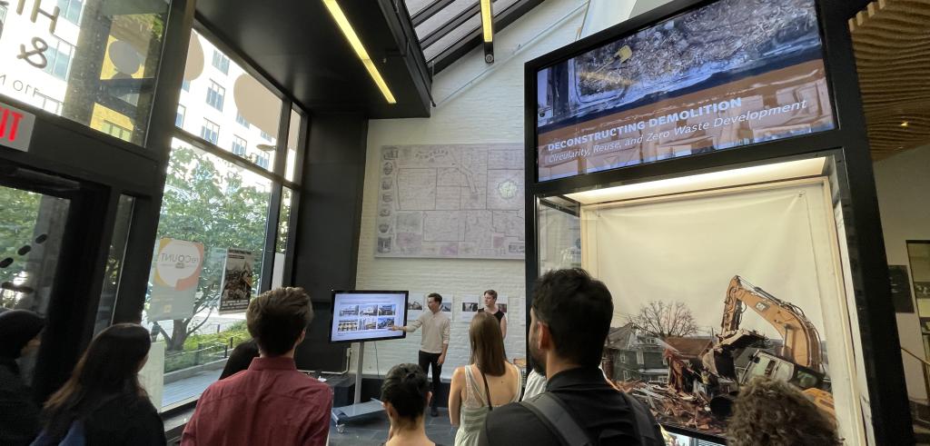 Group of students watching two presenters on deconstruction demolition in an indoor facility with windows. 