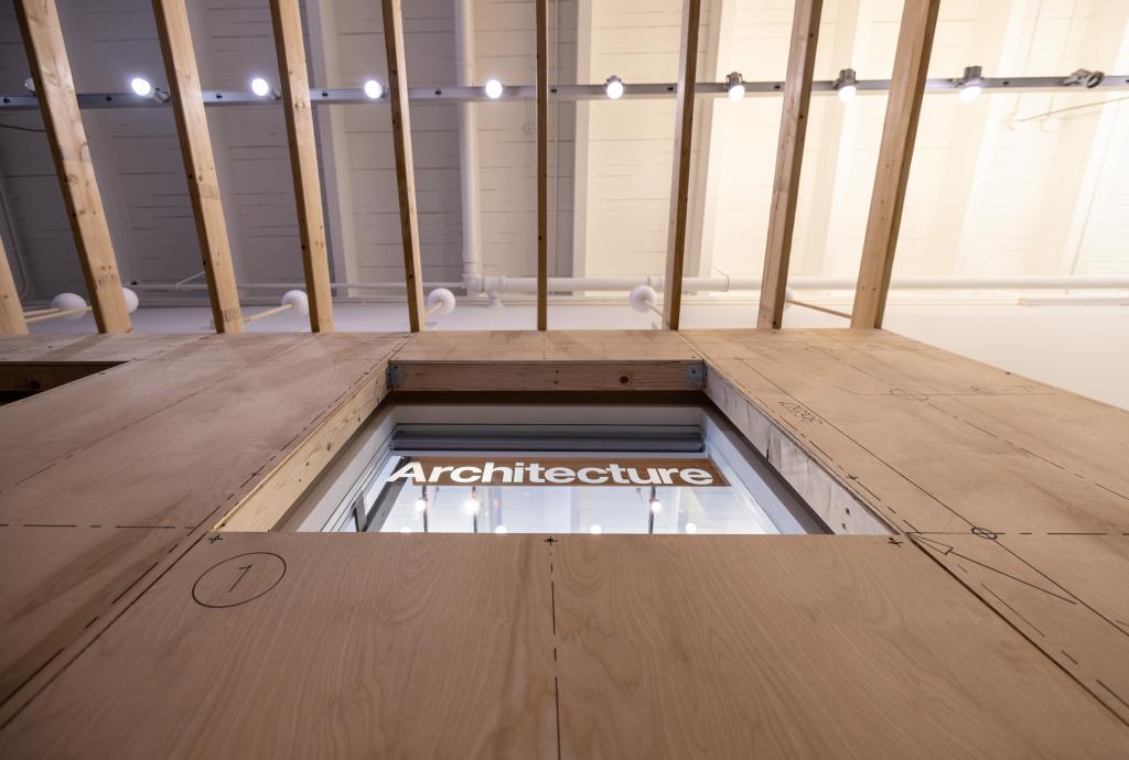 An upwards shot of wood paneling surrounding a window that says ARCHITECTURE and wood beams