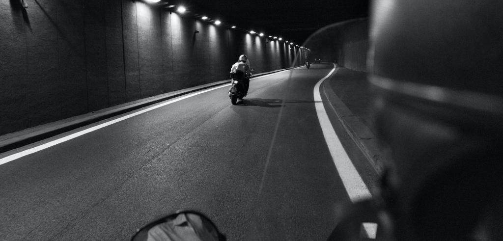 Black and white image of a street and a person driving a moped