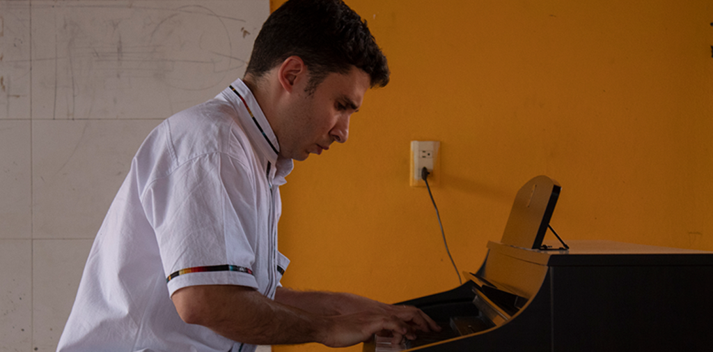 man in white shirt playing the piano with a yellow wall