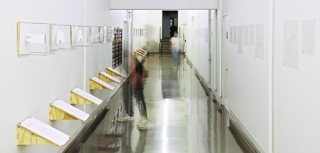 A long exposure of a hallway exhibition space, depicting two blurred people walking between exhibition content.