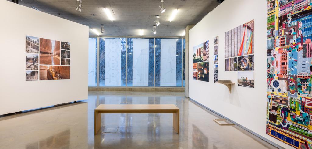 A bench sitting in a gallery space with artwork on the walls with a giant window.