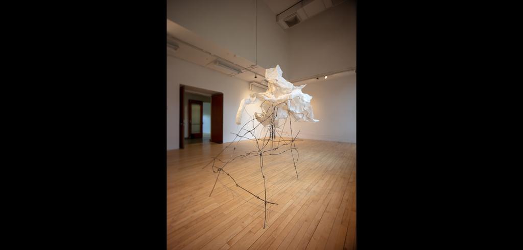 Abstract piece of artwork with white crinkled paper on top of thin black wire in an empty gallery.