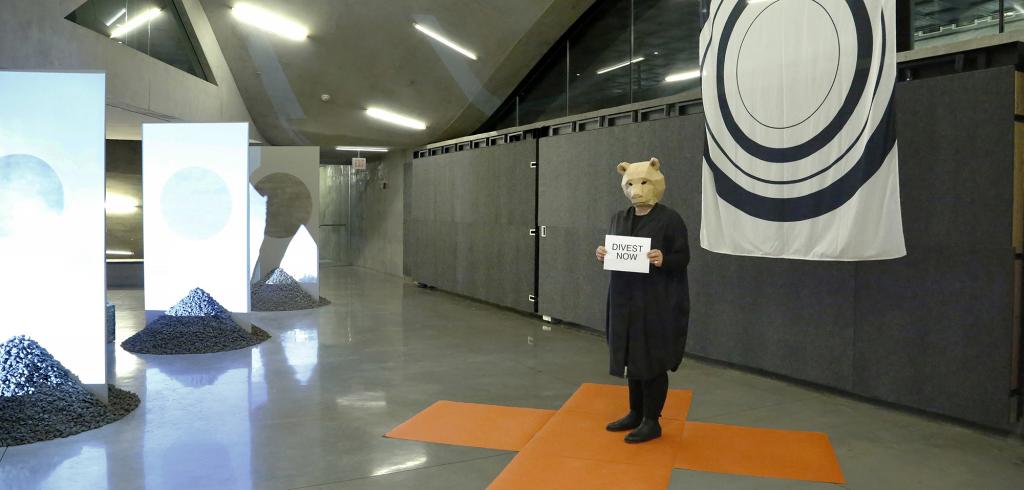 Figure wearing a bear's mask holding a sheet of paper, standing on an orange marker.
