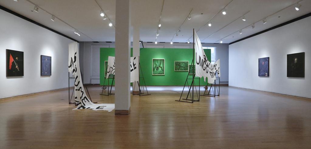 A view of an art gallery with portraits on white walls, steel and cloth sculpture, and green images on a green wall.
