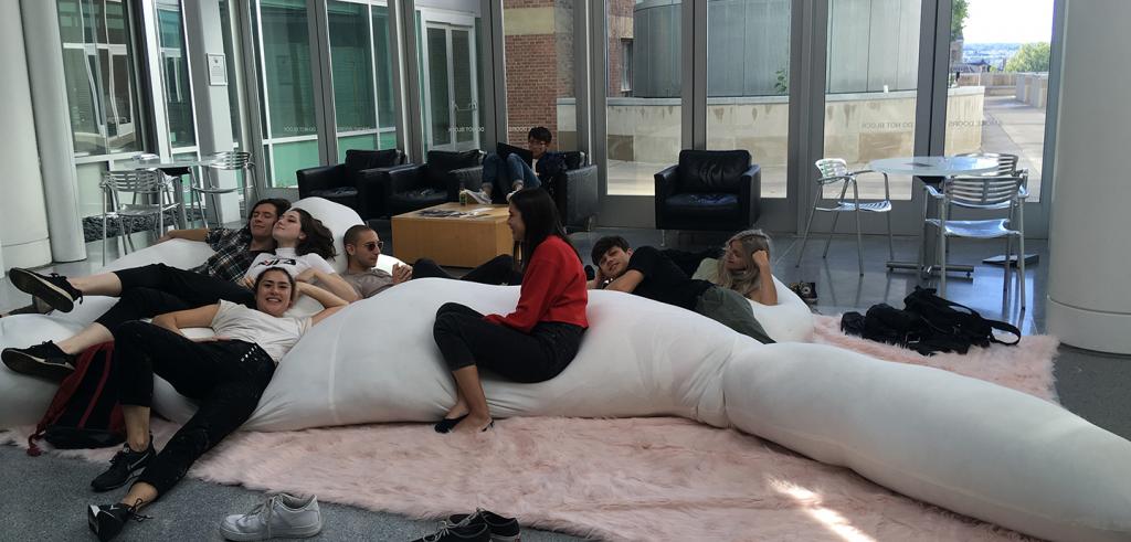 people sitting on a giant white pillow sculpture on a pink rug in a building