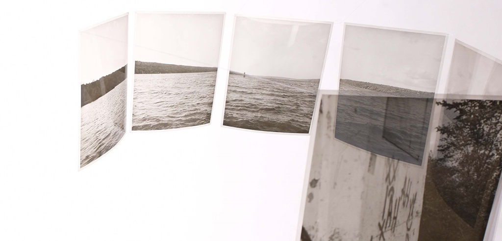Color photo of black and white photos on clear plastic hung in a hexagon shape from the ceiling, on a white background. 