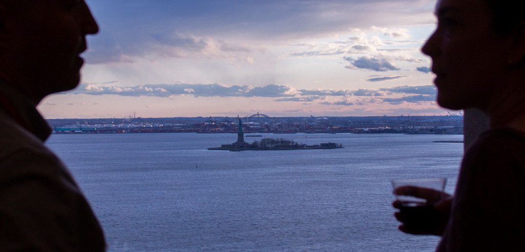 Silhouettes of people in front of the statue of liberty in the distance.