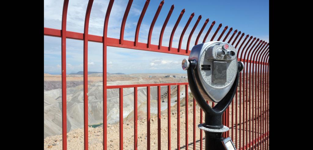A canyon, a red fence, a viewfinder telescope, blue sky.