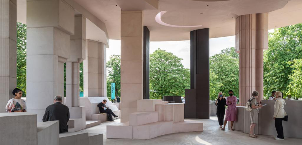 A modern outdoor pavilion structure occupied by eight people, standing underneath. 