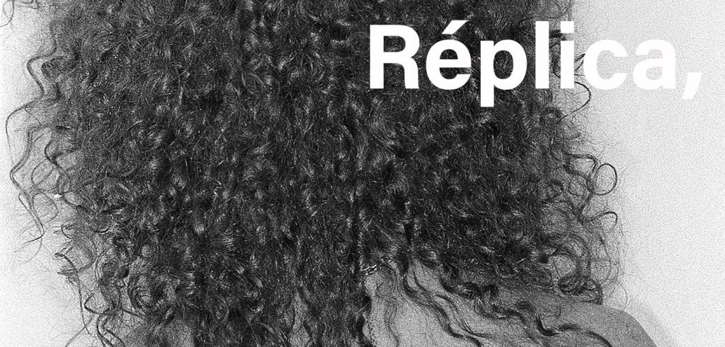 A black and white photograph of the back of someone's head; they have shoulder-length curly and whispy hair with a chain necklace dangling down their back under their hair. In white text on the top right reads 