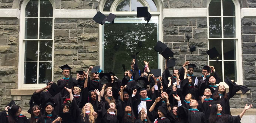 a group of people in graduation robes throwing their caps in the air in front of a stone building with windows