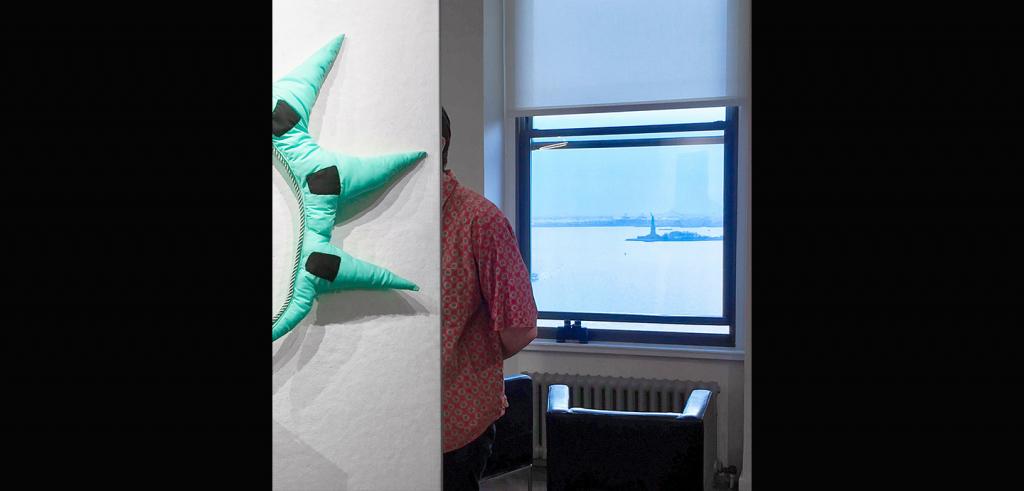 Someone looking at art in an exhibition, with a view of the Statue of Liberty through a window in the background.