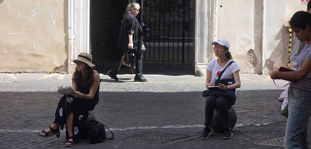 Three women draw in notebooks and a cobblestone street