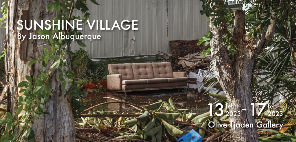 Color photo of a brown couch in standing water, with trees in the foreground and a light grey building in the background. 