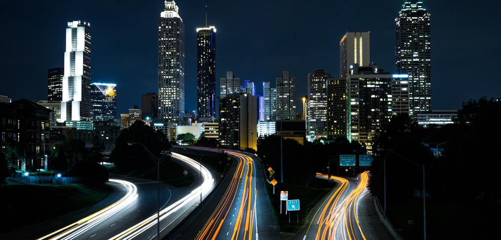 City at night with lights, tall buildings and a highway.