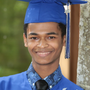 A person wearing a blue graduation cap and gown smiling.