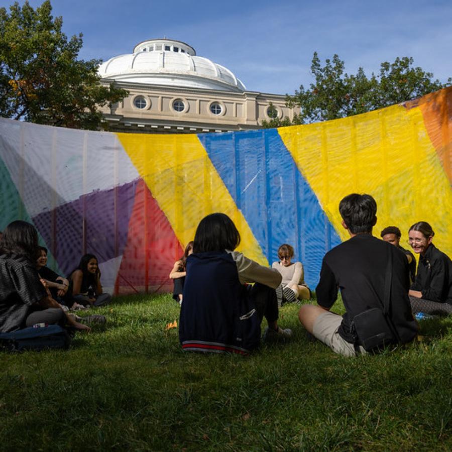 a group of people sitting on the grass surrounded by a colorful barrier